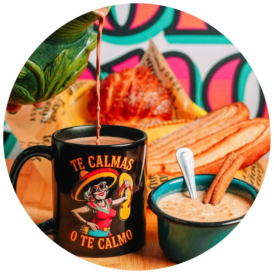 Hot chocolate pouring into a mug, with churros and a bowl of rice pudding with cinnamon sticks.