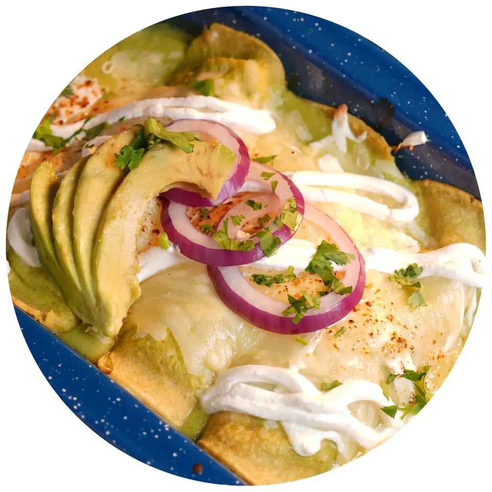 Green enchiladas topped with melted cheese, sour cream, red onion, avocado slices, and cilantro.